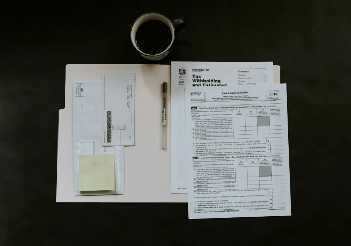 Belastingformulieren, een pen en een koffiemok op een donker bureau